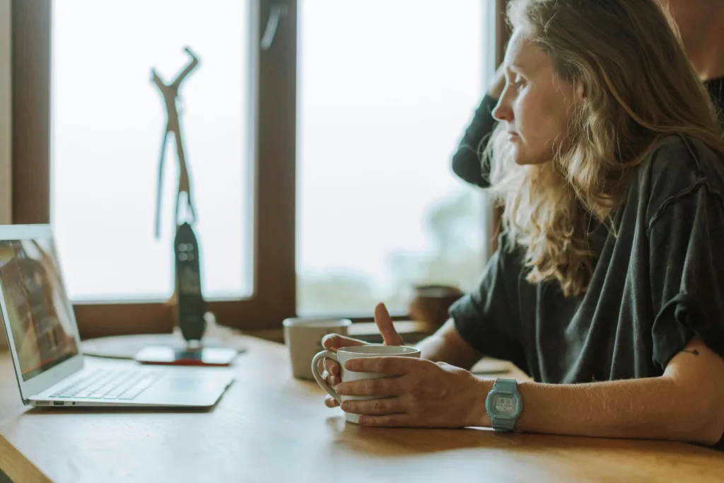 A focused solopreneur sitting at a wooden desk with a laptop and a coffee mug, looking contemplative as they work in a cozy, natural-lit workspace. The image captures the challenges of balancing client work and content marketing, emphasizing the need for consistent content creation to grow a small business.